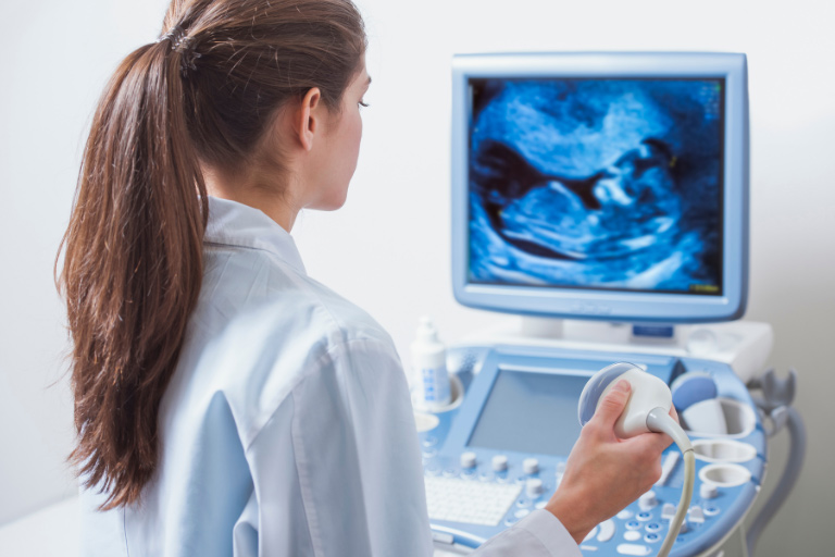 Junge Frau hält Ultraschallsonde und schaut auf Bildschirm eines Ultraschallgeräts.