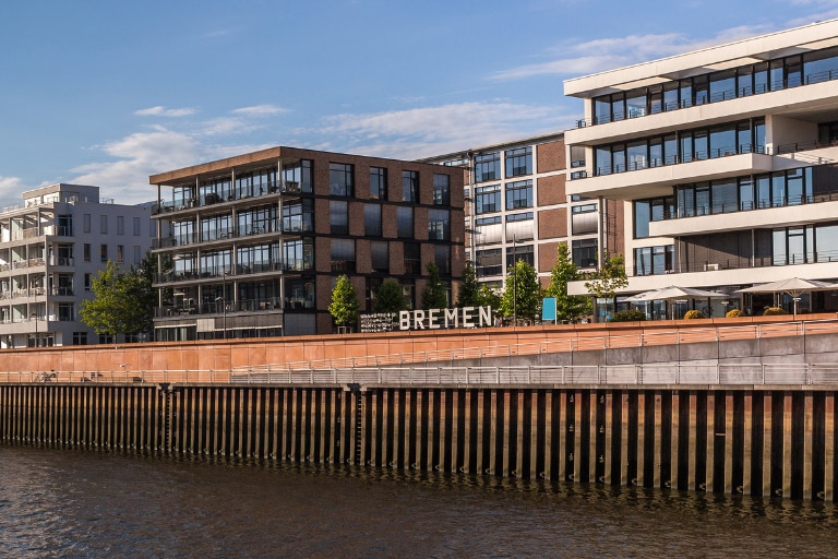 Geschäftsgebäude an der Bremer Weser mit Bremen-Schriftzug an der Uferpromenade bei sonnigem Wetter